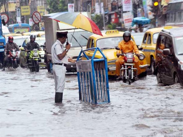 A high-resolution image capturing Kolkata's waterlogged streets during a heavy monsoon downpour. A vintage blue tram is partially submerged in rainwater, surrounded by chaotic traffic and pedestrians carrying umbrellas. The scene reflects the city’s urban struggle with monsoon flooding, set in a moody and cinematic atmosphere.